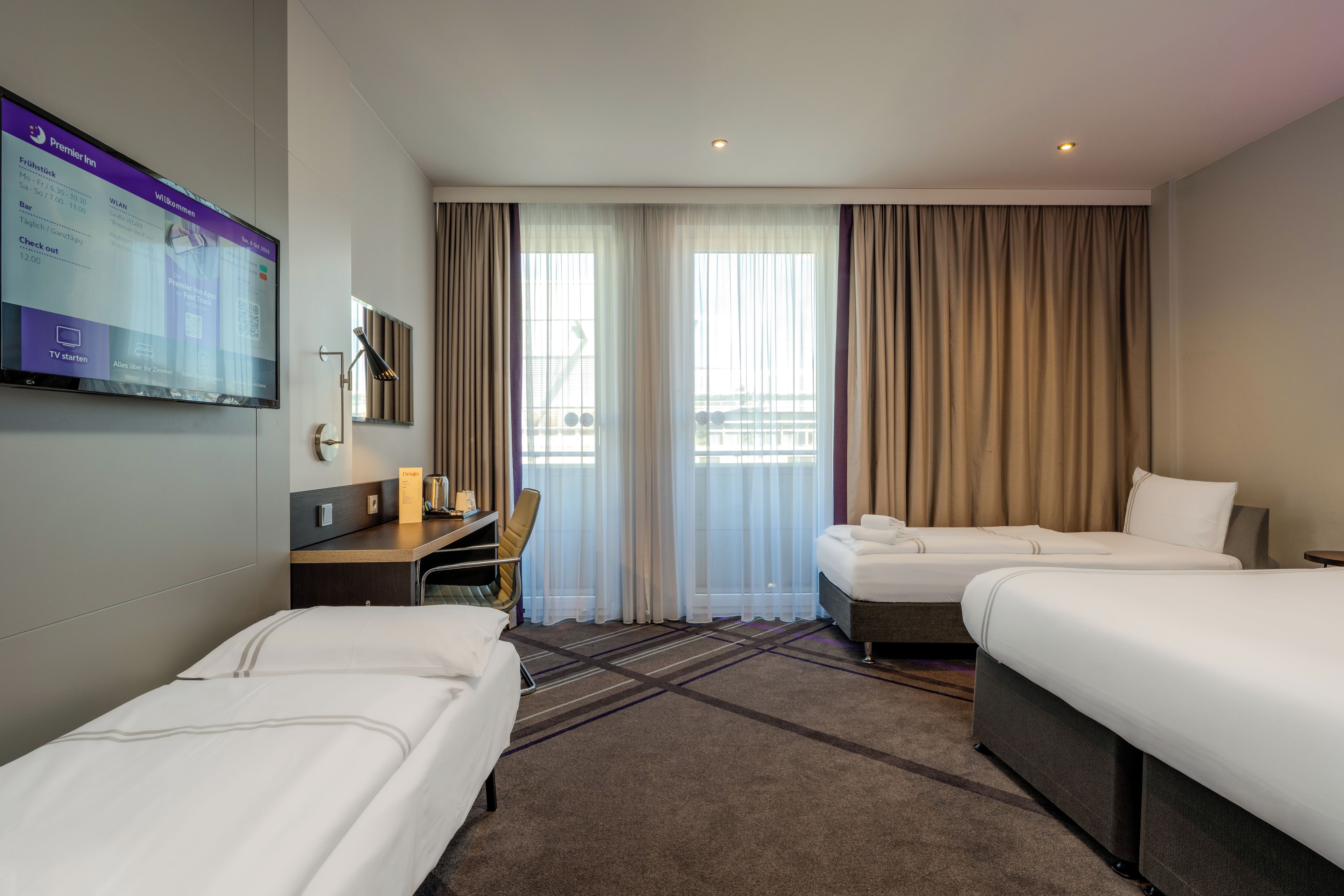 A hotel room with two beds, a desk, a TV, and a window with curtains.