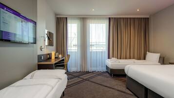 Ein Hotelzimmer mit zwei Betten, einem Schreibtisch, einem Fernseher und einem fenster mit Vorhängen.