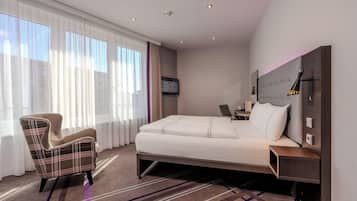 Habitación de hotel con cama, sillón, escritorio y televisor.