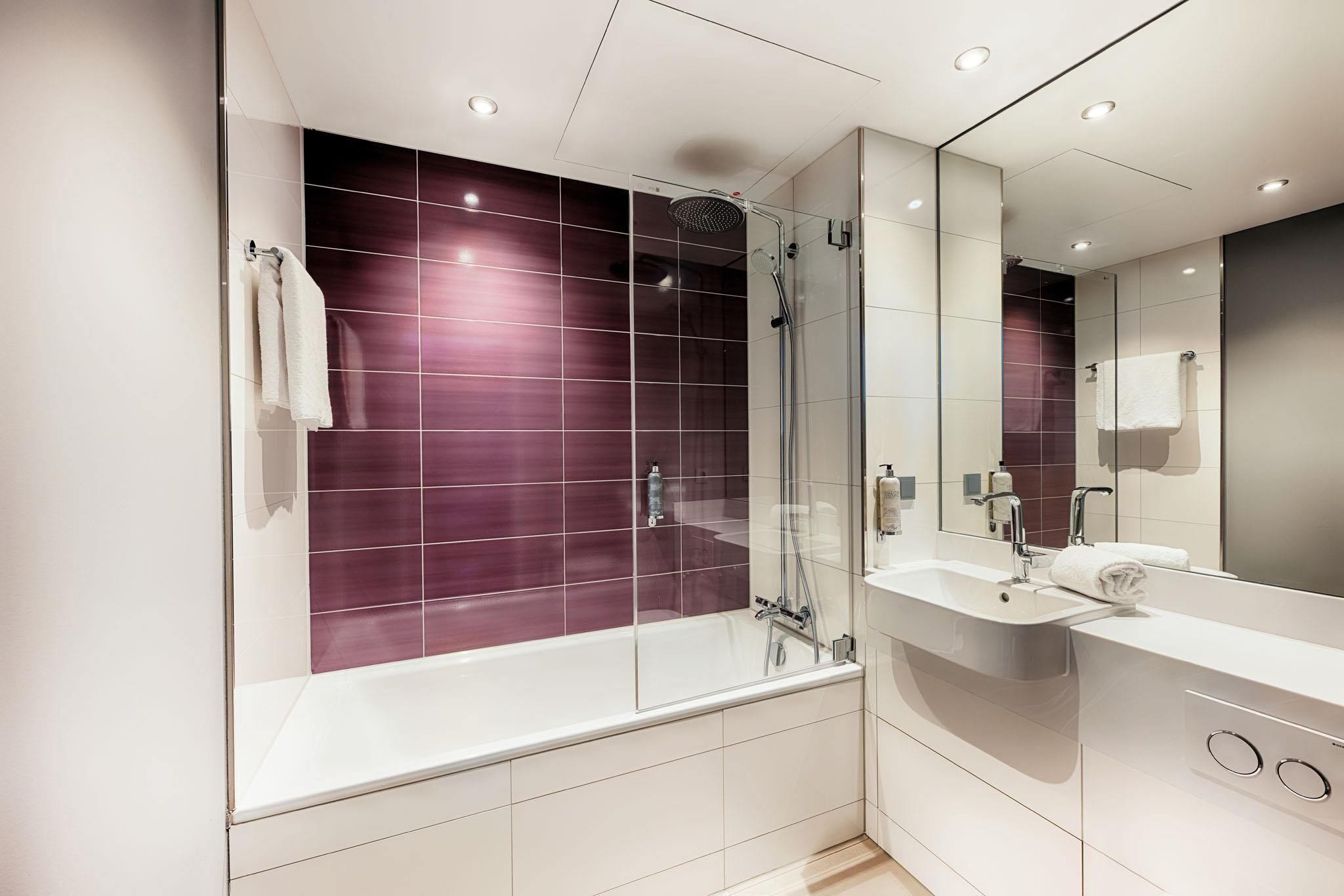 Een moderne badkamer met een douchecabine van glas, een wit bad en een grote spiegel boven de wastafel.