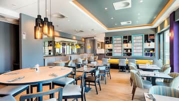 A modern restaurant with round tables, chairs, pendant lighting, and a bookshelf area.