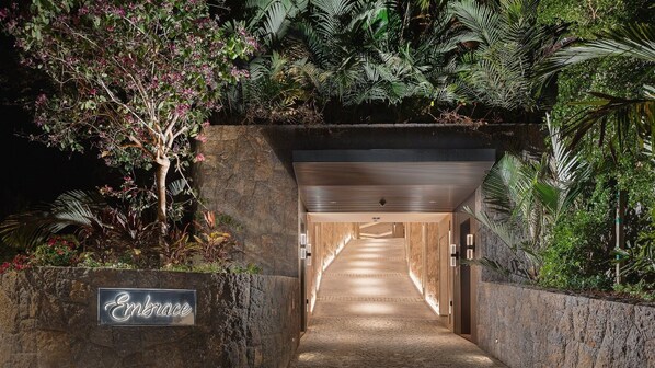 A tunnel entrance with a stone wall, a sign reading "Embrace", and lush greenery on either side.