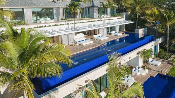 Une maison de luxe moderne dotée d’une grande piscine, d’un espace salon extérieur et d’une végétation luxuriante.