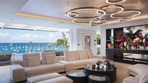 A modern living room with a large sofa, a coffee table, and a view of the sea with boats. - Embrace (2/5 Rooms) Luxury villa (Gustavia)
