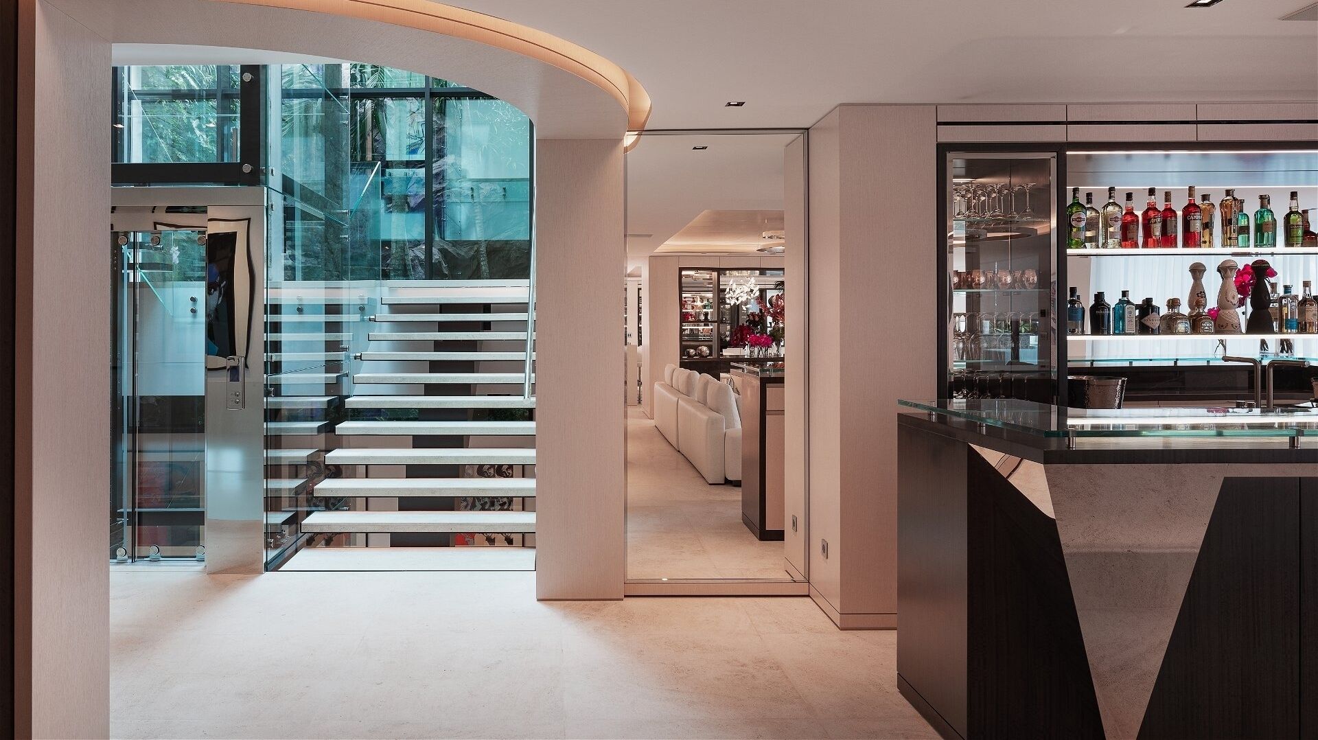 Een modern interieur met een glazen trap, een bar met flessen en een keuken op de achtergrond.