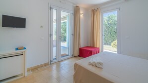 A hotel room with a bed, a TV, a desk, a red table, and a sliding glass door leading to an outdoor area. - Villa 'Melus Maris' with Sea View, Pool, Garden, Terrace & Wi-Fi (Siracusa)