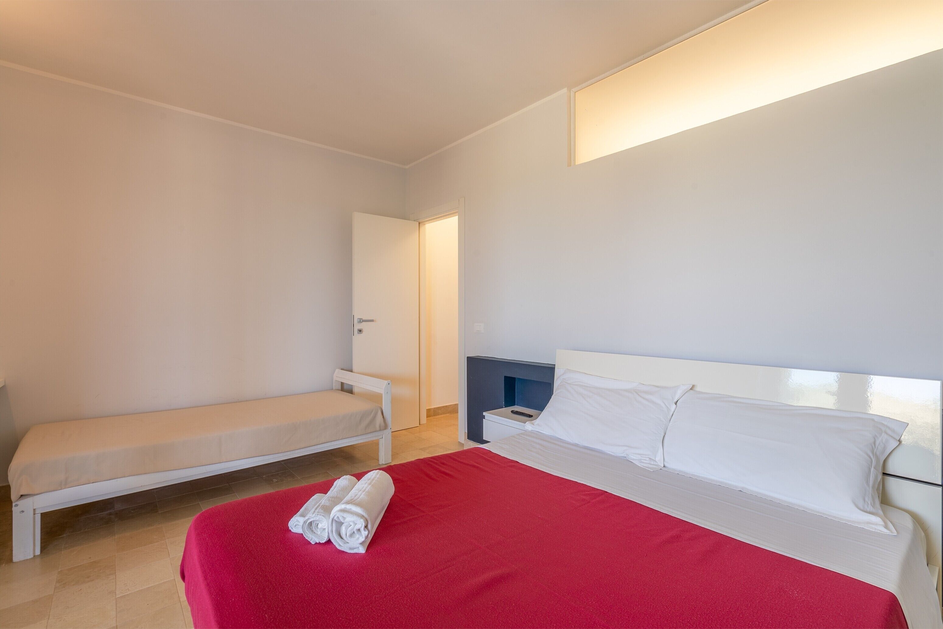 A bedroom with a bed, a bench, a bedside table, and a wall-mounted light.