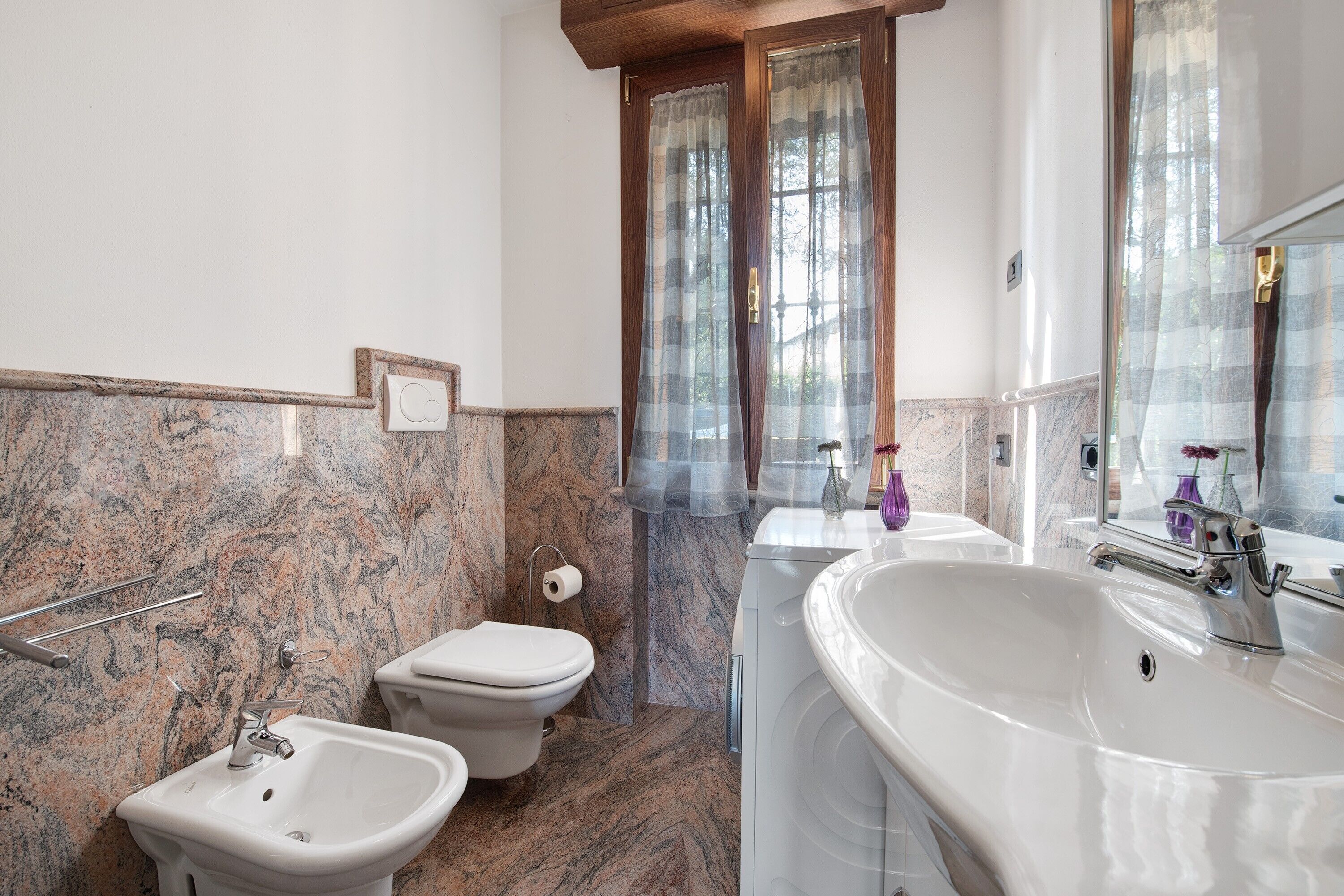 A bathroom with a marble wall, a toilet, a bidet, and a sink.