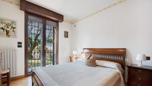 Un dormitorio con una cama grande, cabecera de madera, una mesita de noche con lámpara, una silla y un radiador.
