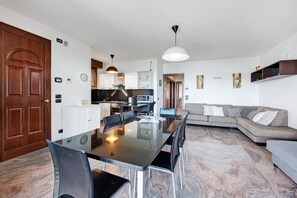 Une cuisine moderne avec des meubles blancs, une table à manger avec des chaises, un canapé et une grande porte en bois.