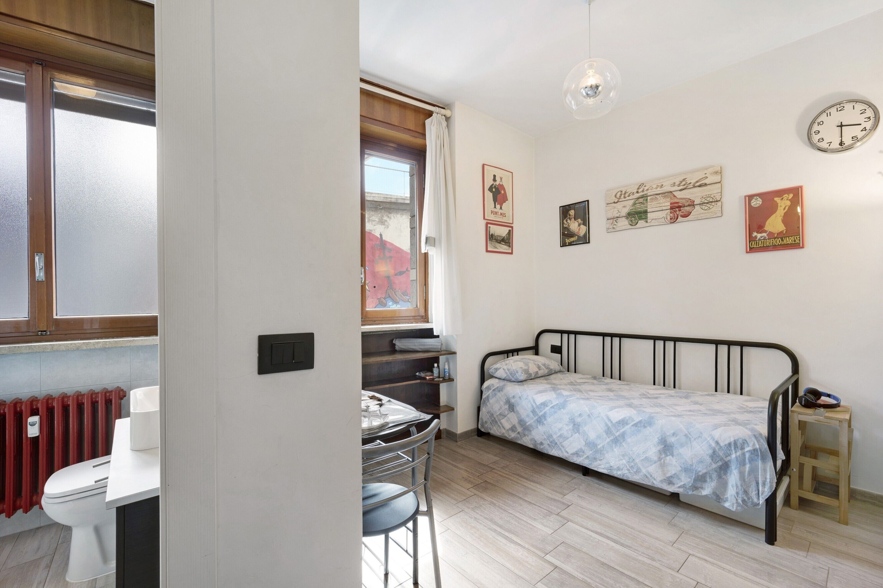 A bedroom with a bed, a desk, a chair, a radiator, and a window.