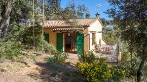 Una casa rústica con techo de tejas, contraventanas verdes y un patio con mobiliario exterior.
