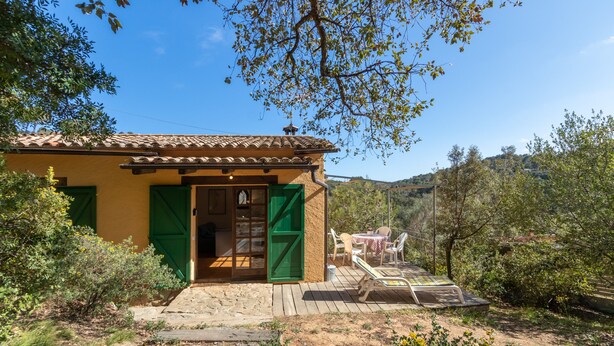 Un edificio rústico con techo de tejas, terraza de madera y puerta verde.