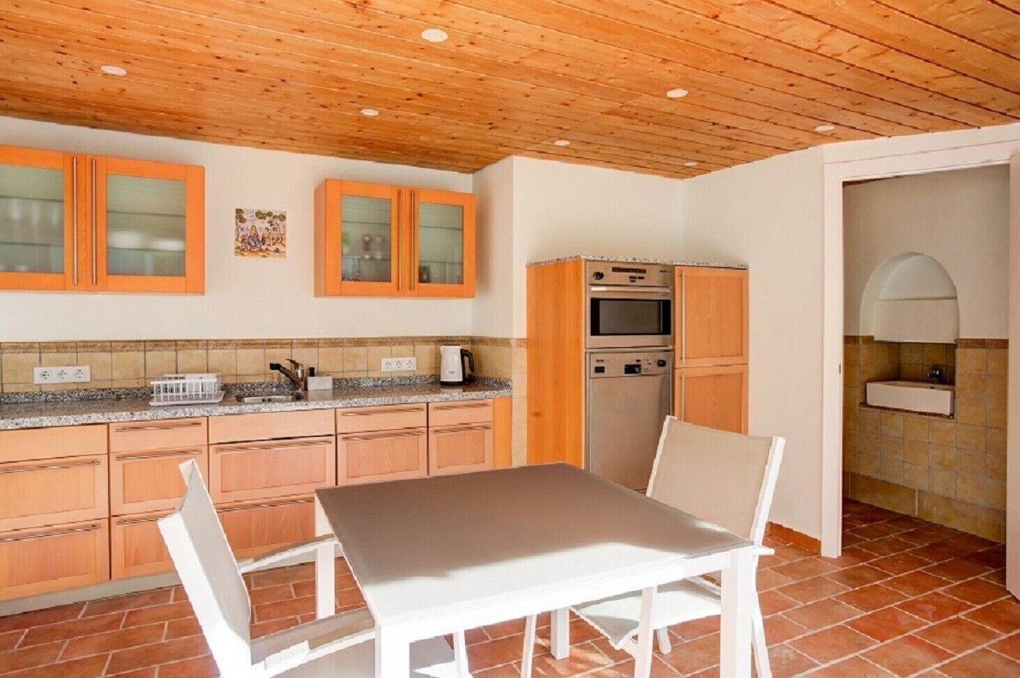 A kitchen with wooden cabinets, a countertop, a table, chairs, an oven, and a sink.