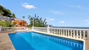 Une piscine dotée d’une balustrade blanche, entourée d’une clôture blanche, d’où l’on peut admirer un bâtiment rouge et des arbres en arrière-plan.