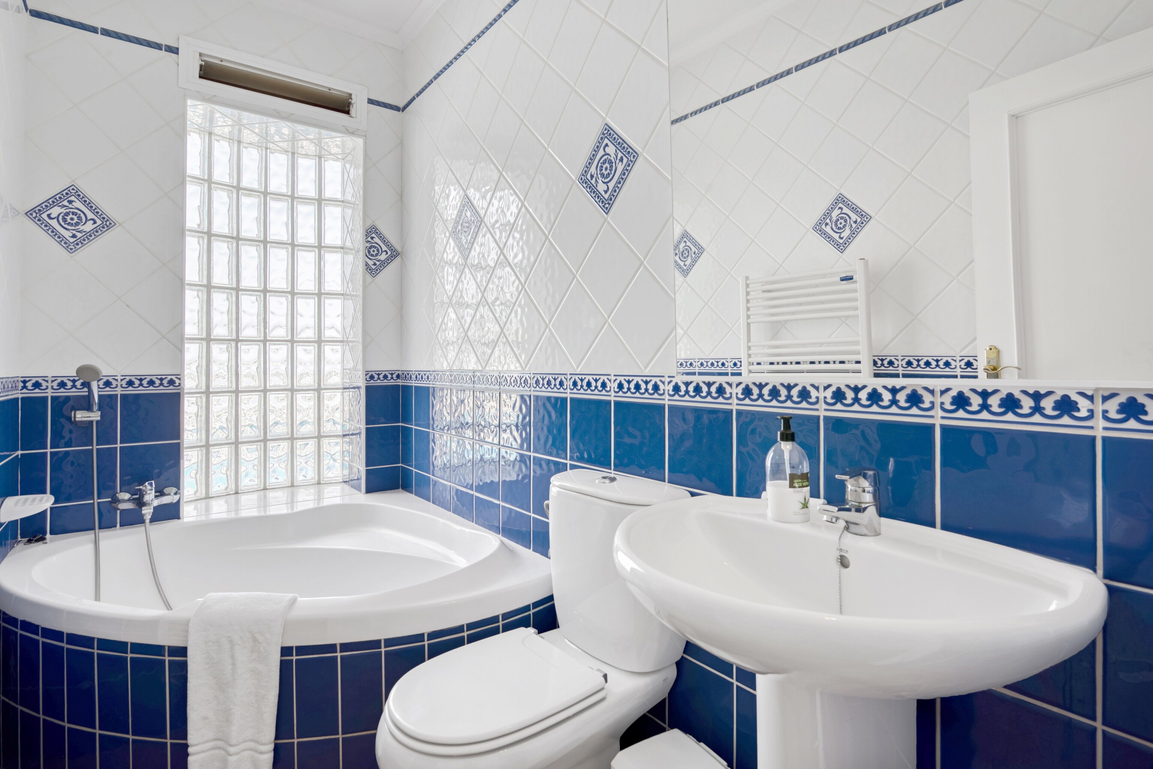A bathroom with a bathtub, toilet, and sink, featuring blue and white tiles and a window.