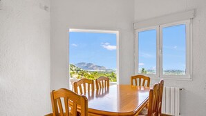 Un espace repas avec une table et des chaises en bois, de grandes fenêtres offrant une vue sur les montagnes et la verdure.