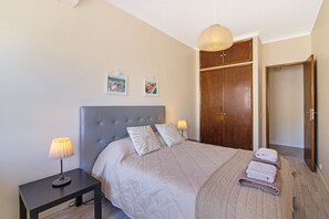 A bedroom with a bed, bedside lamps, a nightstand, a wardrobe, and a door.