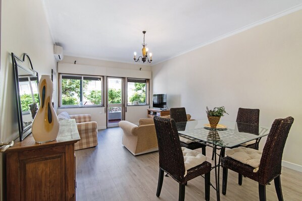 A dining area with a glass table, wicker chairs, a sofa, and a television in the background.