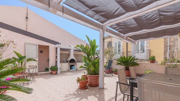 An outdoor patio area with a grill, potted plants, and a covered seating area.