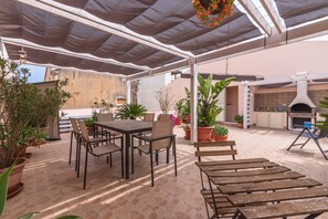 Un patio al aire libre con una mesa y sillas, rodeado de plantas en macetas.