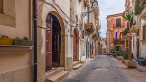 A narrow cobblestone street lined with historic buildings, featuring arched doorways and traditional architecture.