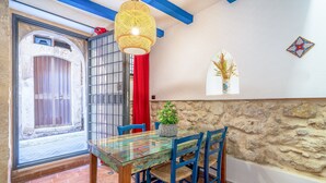A dining area with a glass table, blue chairs, a hanging light fixture, and a stone wall.