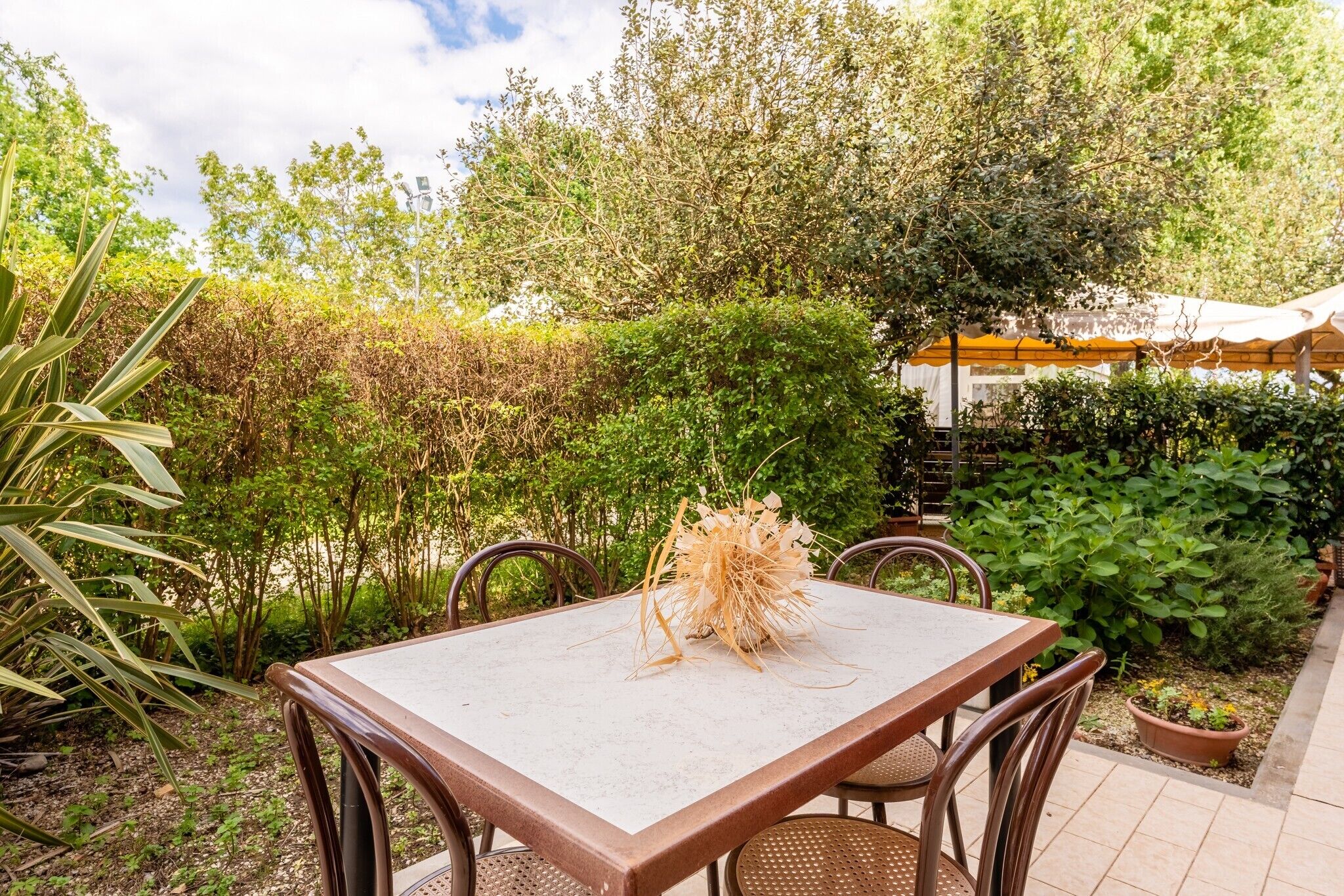Un patio al aire libre con una mesa y sillas, rodeado de follaje y una pérgola.