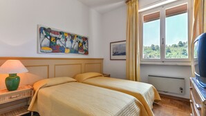 Une chambre d’hôtel avec deux lits, un tableau, une fenêtre avec des rideaux, une lampe et un téléviseur.