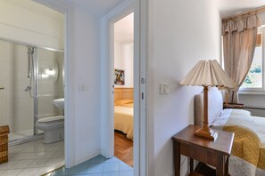 A bathroom with a glass-enclosed shower, a toilet, and a bed with a yellow blanket.