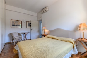 Um quarto com uma cama, uma cadeira, uma mesinha e um abajur.