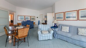 Un salon comprenant une table à manger, des chaises, un canapé et un fauteuil à rayures bleues. On peut y voir des tableaux encadrés accrochés au mur, une lampe posée sur une table d’appoint et un meuble bleu.