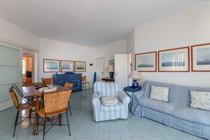 Un salon comprenant une table à manger, des chaises, un canapé et un fauteuil à rayures bleues. On peut y voir des tableaux encadrés accrochés au mur, une lampe posée sur une table d’appoint et un meuble bleu.