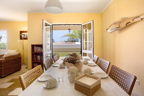 An open dining area with a view of the outdoors, a bookshelf, wicker chairs, and a table set for dining.