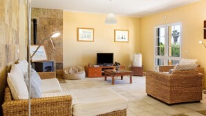 A living room with wicker furniture, a television, and framed pictures on the wall. - Villa 'Retiro Praia' with Mountain View, Private Terrace and Wi-Fi (Campo de Baixo)