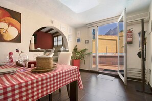 Comedor con mantel a cuadros, planta en maceta y vista a un paisaje montañoso a través de una puerta abierta.