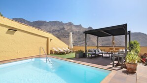 A swimming pool with lounge chairs and a covered seating area, with mountains in the background. - Holiday Home 'La Suerte' with Sea View, Wi-Fi and Air Conditioning (Agaete)