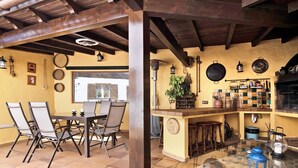 A dining area with a table and chairs, a bar with stools, and a kitchen area with shelves and utensils. - Holiday Home "Los Veroles" with Sea View, Private Heated Pool and Wi-Fi (Agaete)