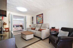 Un salon comprenant un canapé, un pouf et un fauteuil en cuir noir. On y trouve également une table basse en bois, une petite table d’appoint et un tableau encadré accroché au mur.