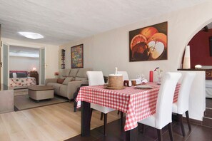 Un coin repas avec une nappe à carreaux, des chaises blanches et un tableau accroché au mur.