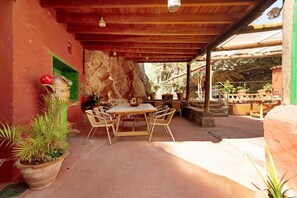 Une terrasse extérieure avec une table et des chaises en bois, entourée de plantes en pot et d’un mur de pierre.
