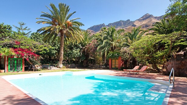 A swimming pool with a mountain backdrop, surrounded by lush greenery and palm trees. - "La Casa Del Molino De Viento" with Mountain Views, Private Heated Pool and Wi-Fi (Agaete)