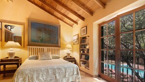 A bedroom with a bed, two bedside tables, a large painting, a bookshelf, and a view of a swimming pool. - "La Casa Del Molino De Viento" with Mountain Views, Private Heated Pool and Wi-Fi (Agaete)