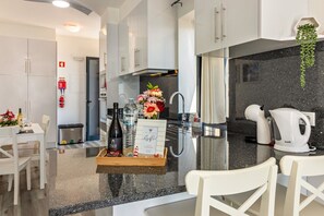 Une cuisine moderne avec des armoires blanches, un comptoir en granit, un four encastré et une machine à café.