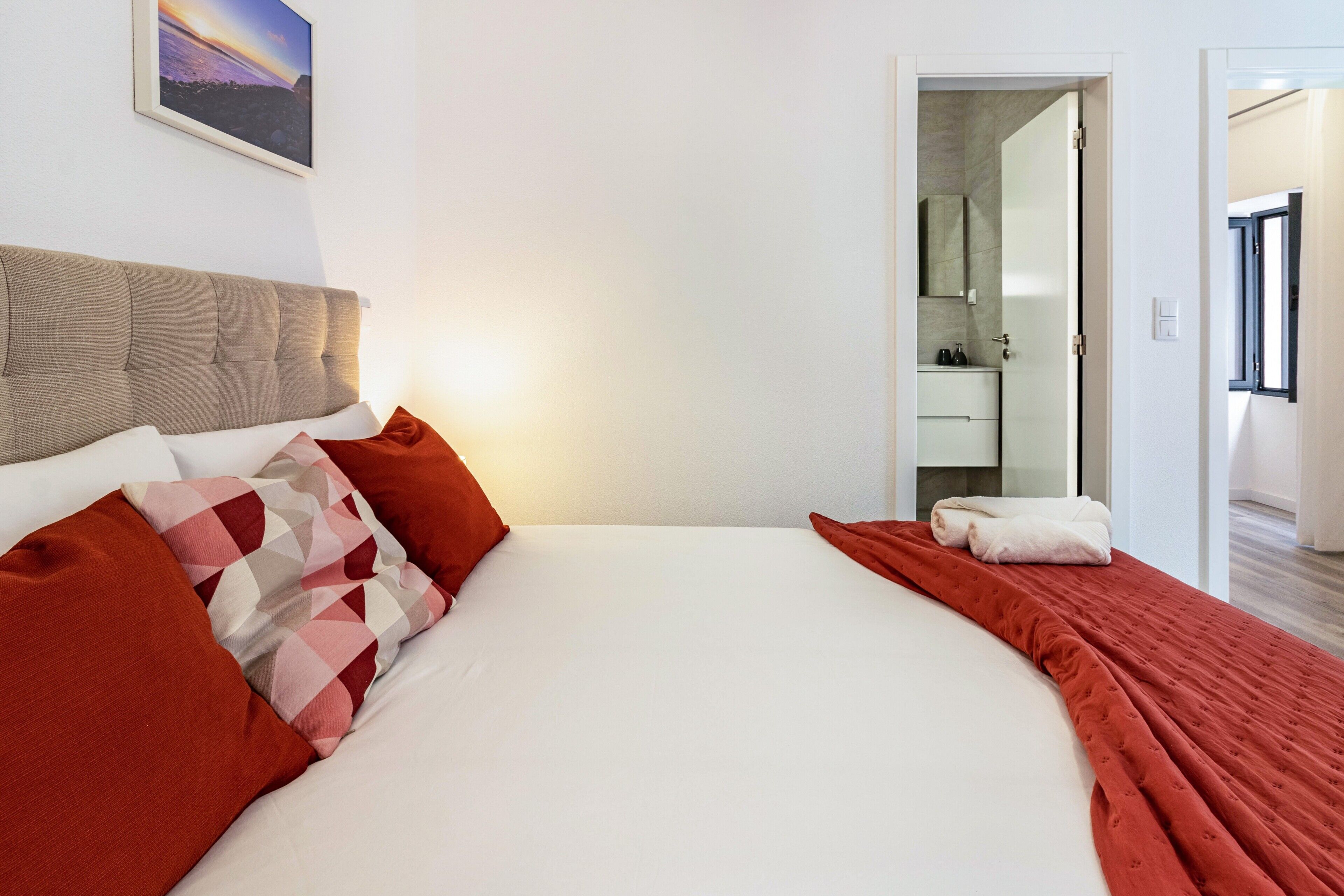 Camera d'albergo con un letto, cuscini, una coperta, un quadro appeso al muro e un bagno visibile attraverso una porta aperta.