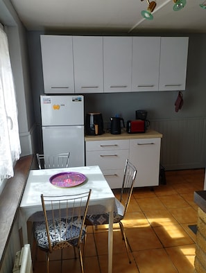 Eine kleine Küche mit weißen Schränken, einem Kühlschrank, einer Kaffeemaschine und einem Toaster.