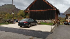 A black car parked in front of a rustic barn-like building with a sloped roof, surrounded by a gravel driveway and a grassy area.