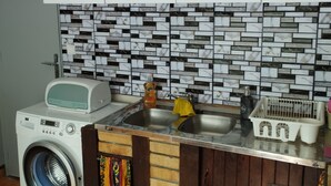 A kitchen with white cabinets, a washing machine, a microwave, a sink, and a tiled backsplash.