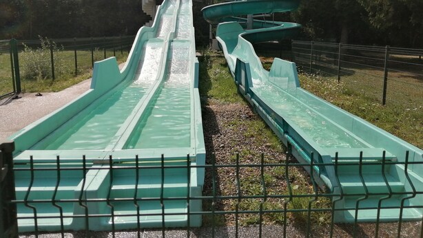 A water slide with multiple lanes, surrounded by a fenced area and trees.