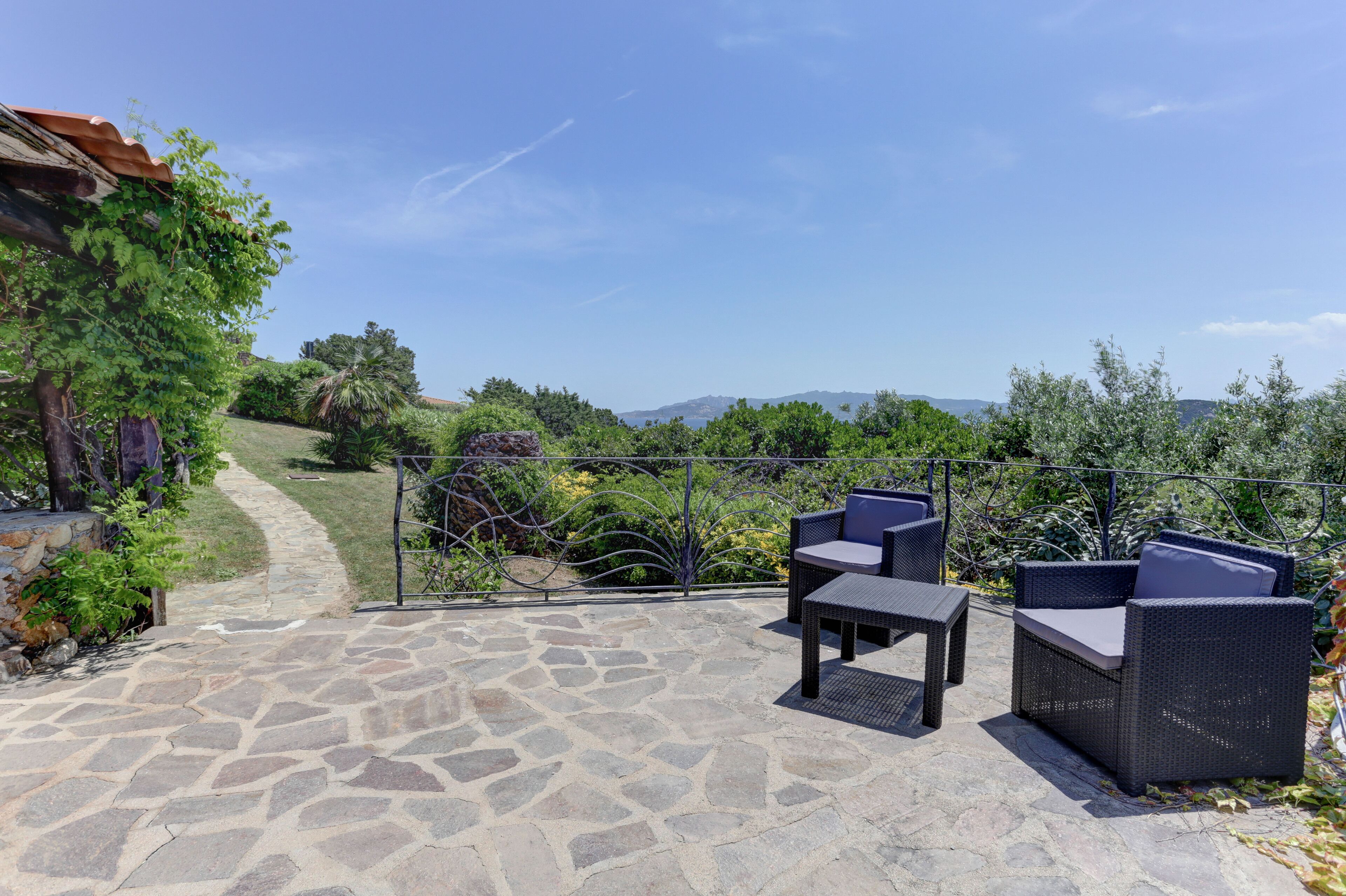 Un patio con suelo de piedra, mobiliario de mimbre y vistas a un paisaje montañoso.